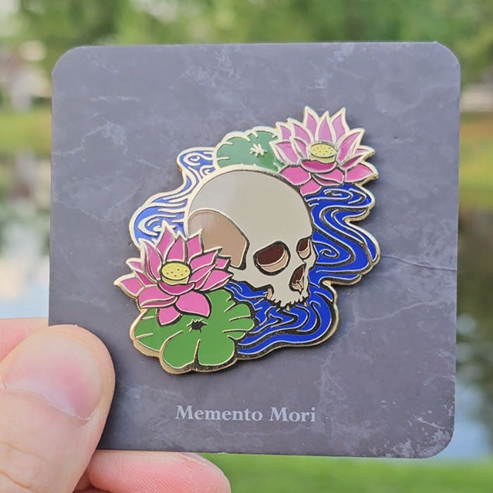 Gold hard enamel pin featuring a pair of lotuses and an emerging skull
