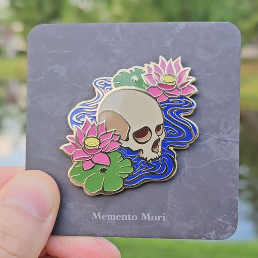 Gold hard enamel pin featuring a pair of lotuses and an emerging skull