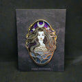An enamel pin featuring a dark fantasy female figure with long wavy hair, a crescent moon and star crown, and a cloud-like patterned bodice, mounted on a dark gray card labeled 'DARK PANTHEON' against a dark background.