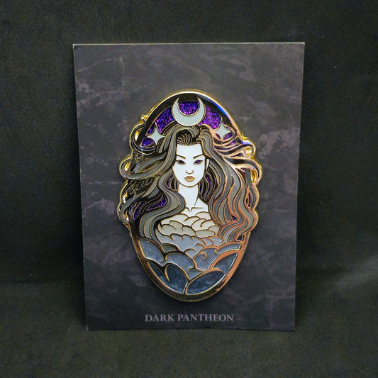An enamel pin featuring a dark fantasy female figure with long wavy hair, a crescent moon and star crown, and a cloud-like patterned bodice, mounted on a dark gray card labeled 'DARK PANTHEON' against a dark background.