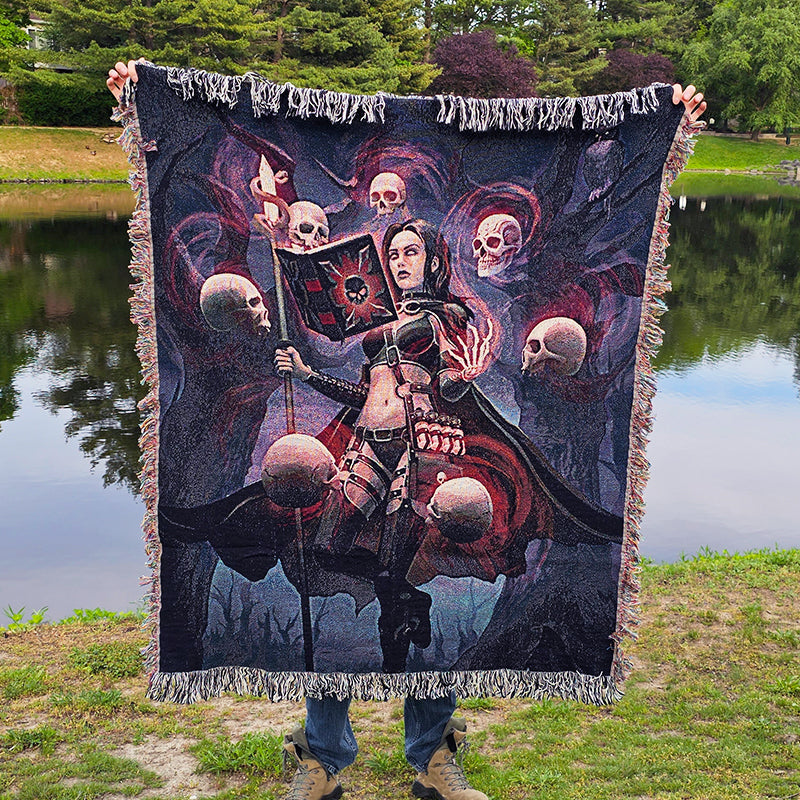 Person holding a large tapestry with a fantasy design featuring a woman and skulls by a lake.